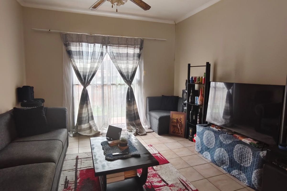 A living room featuring tiled flooring, a ceiling fan, and sliding glass doors providing access to the exterior.