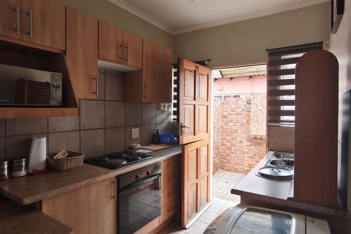 Compact kitchen featuring wood-look cabinetry, built-in oven and hob, tiled flooring, and direct access to an enclosed rear courtyard area.