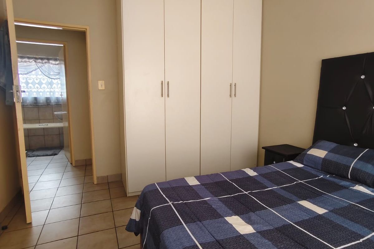 A bedroom featuring built-in cupboards and tiled flooring, with an adjoining bathroom visible through the doorway.