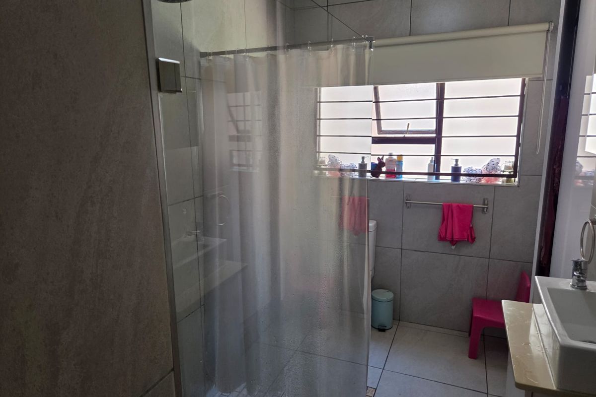 A functional bathroom featuring large-format grey wall and floor tiles, a glass-enclosed shower with a rainfall showerhead, and a wall-mounted vanity basin.