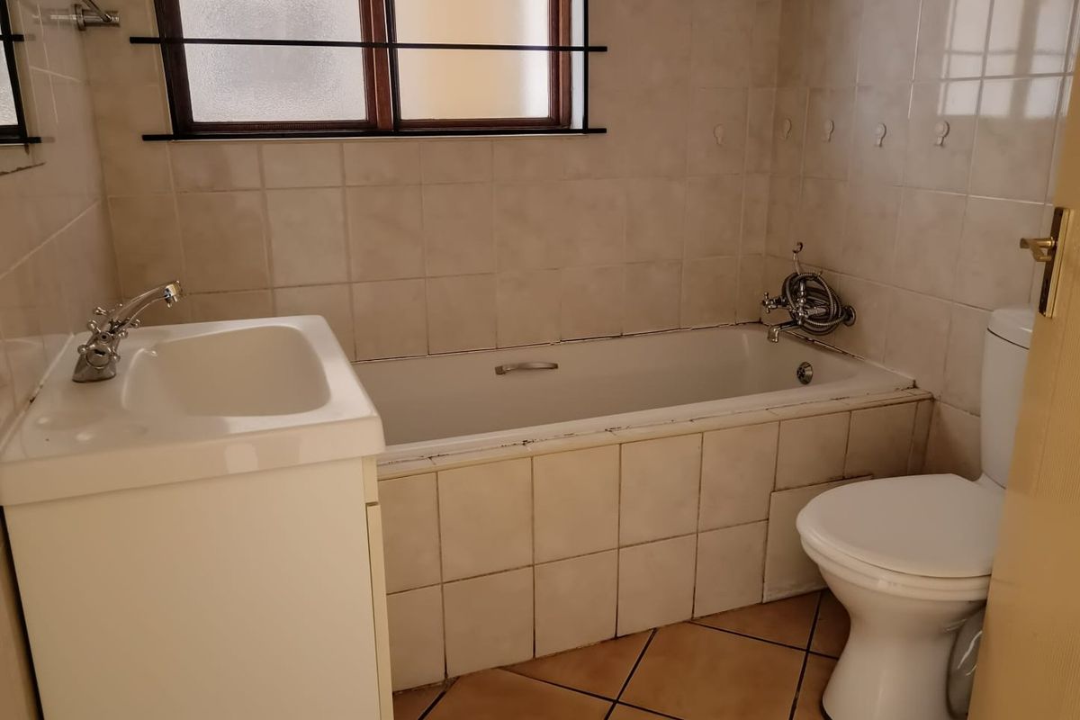A functional bathroom featuring a built-in bathtub with shower mixer, pedestal basin, and toilet, finished with neutral wall tiles and floor tiling.