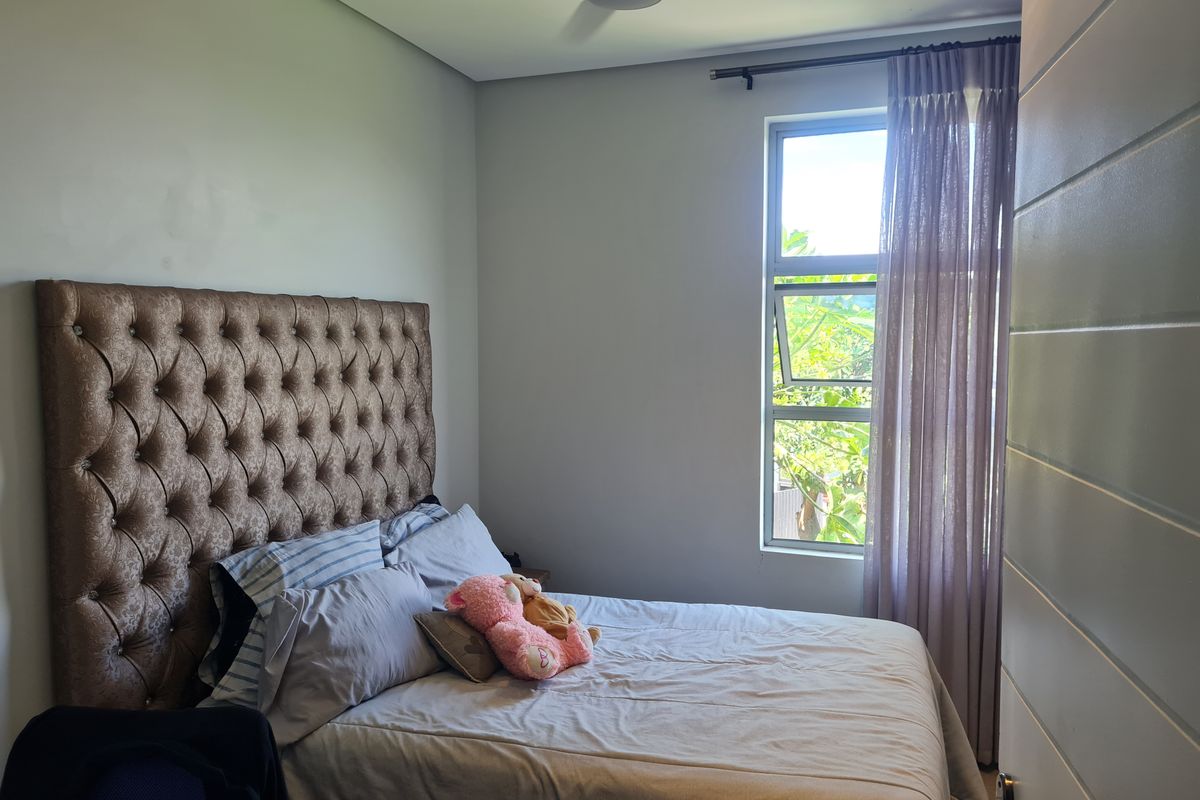 A well-maintained bedroom featuring a ceiling fan, neutral wall finishes, and a large window providing natural light.