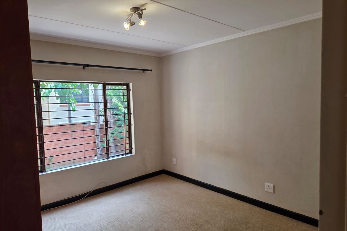 A vacant bedroom featuring neutral carpeting, a window with security bars, and a ceiling-mounted light fixture.