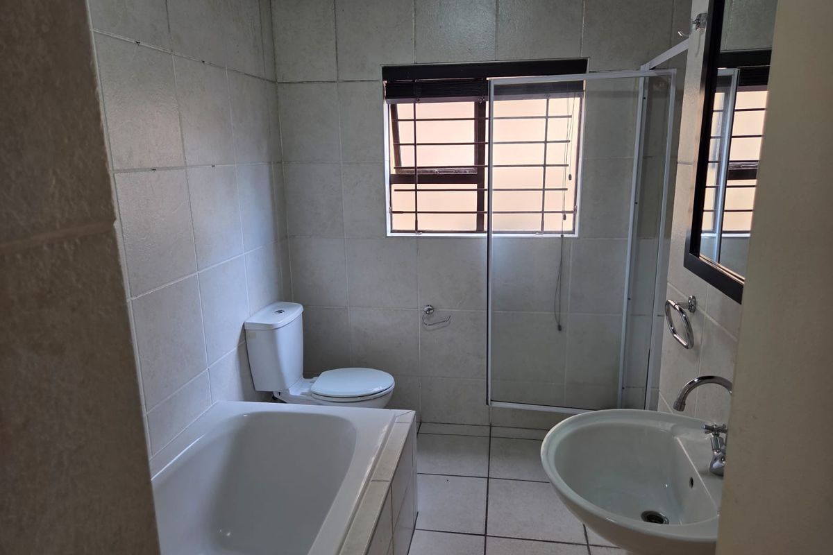 A functional bathroom featuring a built-in bathtub, a separate glass-enclosed shower, a pedestal basin, and a toilet with full-height wall tiling.