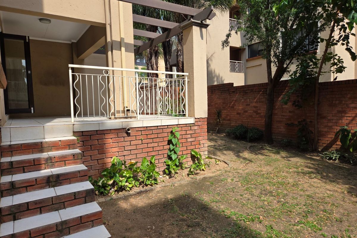 A private ground-floor patio area featuring a pergola, tiled steps, and a small garden space with a brick boundary wall.