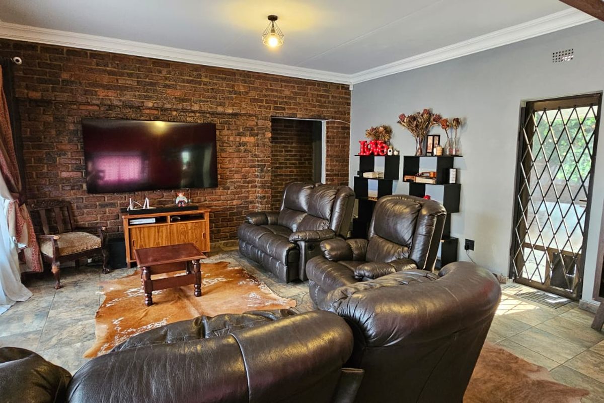 Spacious living room featuring a prominent exposed brick feature wall, tiled flooring, and a security gate leading to the exterior.