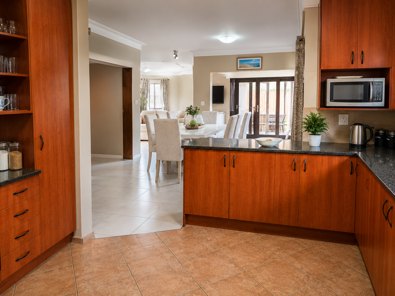 Open-plan kitchen featuring warm-toned wooden cabinetry, granite countertops, and built-in appliances, flowing seamlessly into the adjacent dining and living areas.