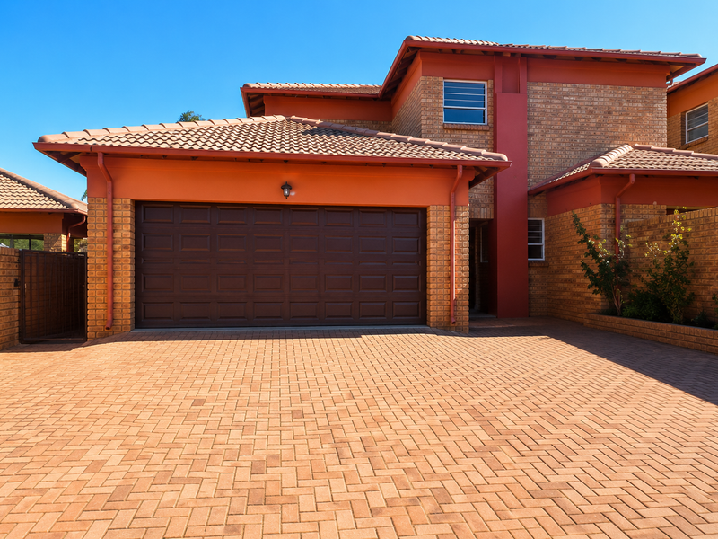 Front view of a double-story brick house featuring a paved driveway, a double garage, and a secure gated entrance.
