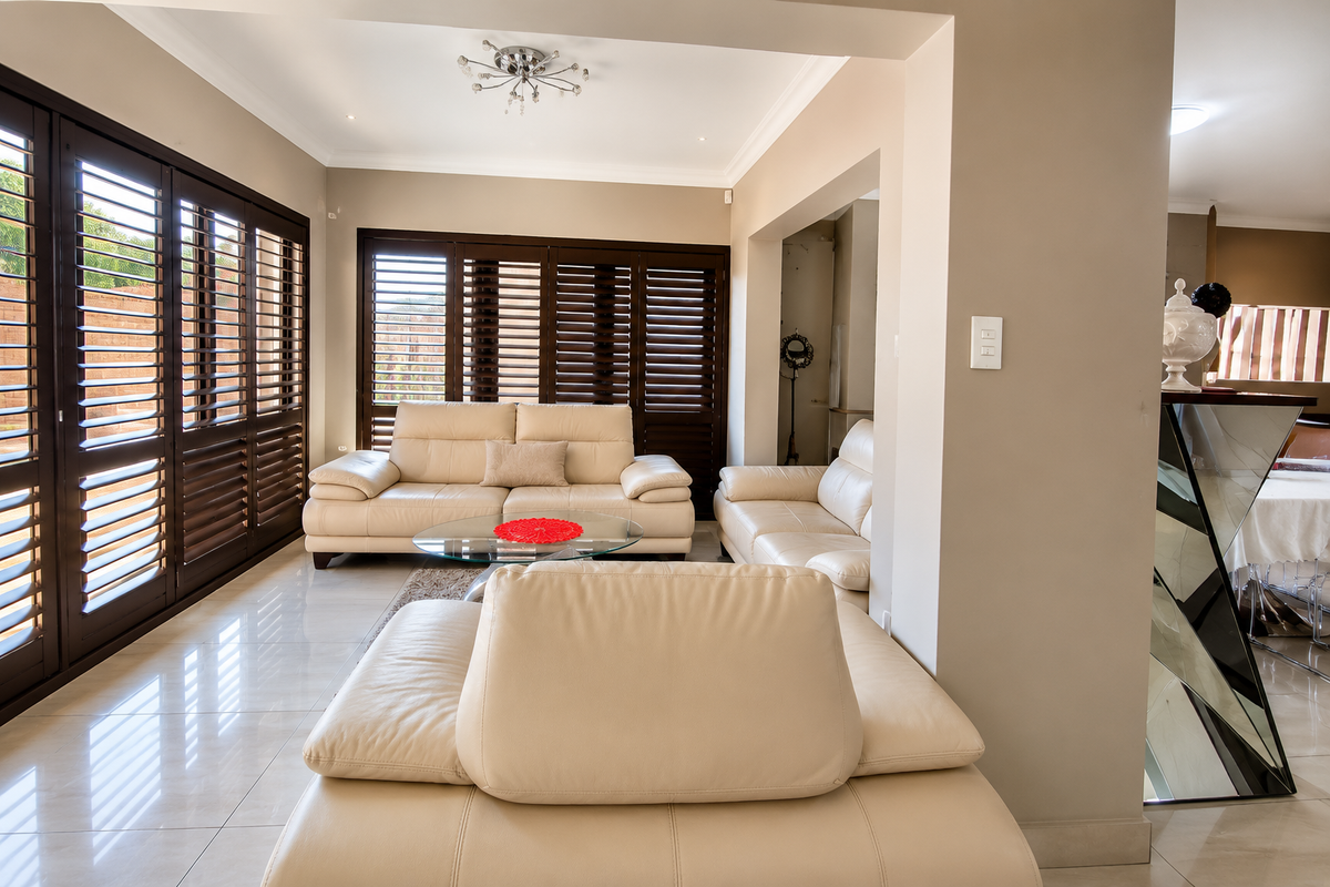Spacious living room featuring polished tiled flooring, recessed downlighting, and dark timber plantation shutters providing natural light control.