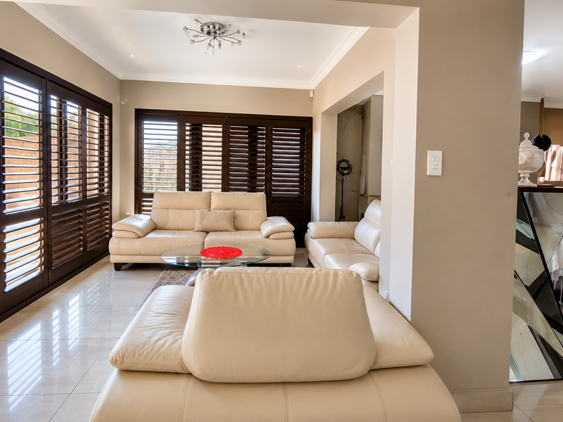 Spacious living room featuring polished tiled flooring, recessed downlighting, and dark timber plantation shutters providing natural light control.