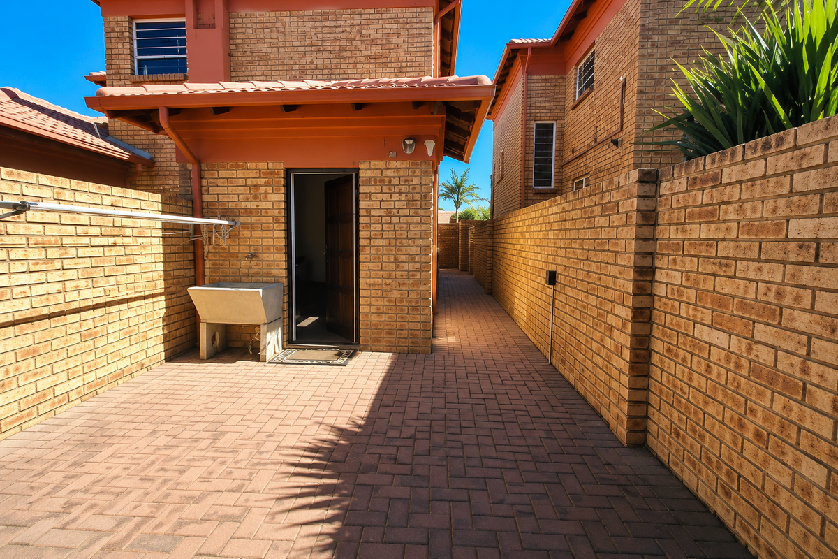 A private rear courtyard featuring paved flooring, brick boundary walls, a utility sink, and a wall-mounted clothesline.