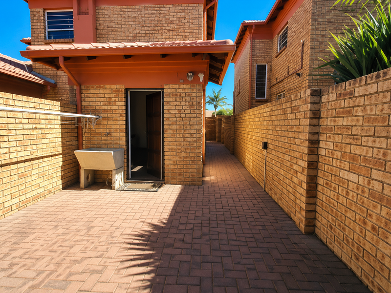 A private rear courtyard featuring paved flooring, brick boundary walls, a utility sink, and a wall-mounted clothesline.