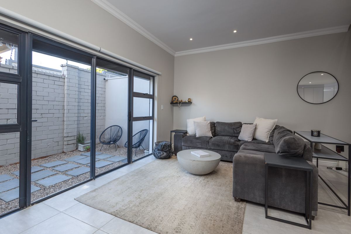 A bright living room featuring large sliding glass doors that open onto a private courtyard, complemented by modern tiled flooring and recessed lighting.
