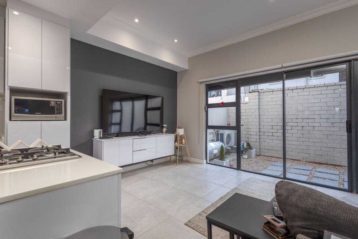 Modern open-plan living area featuring a sleek kitchen with built-in appliances, tiled floors, and large sliding doors opening to a private courtyard.
