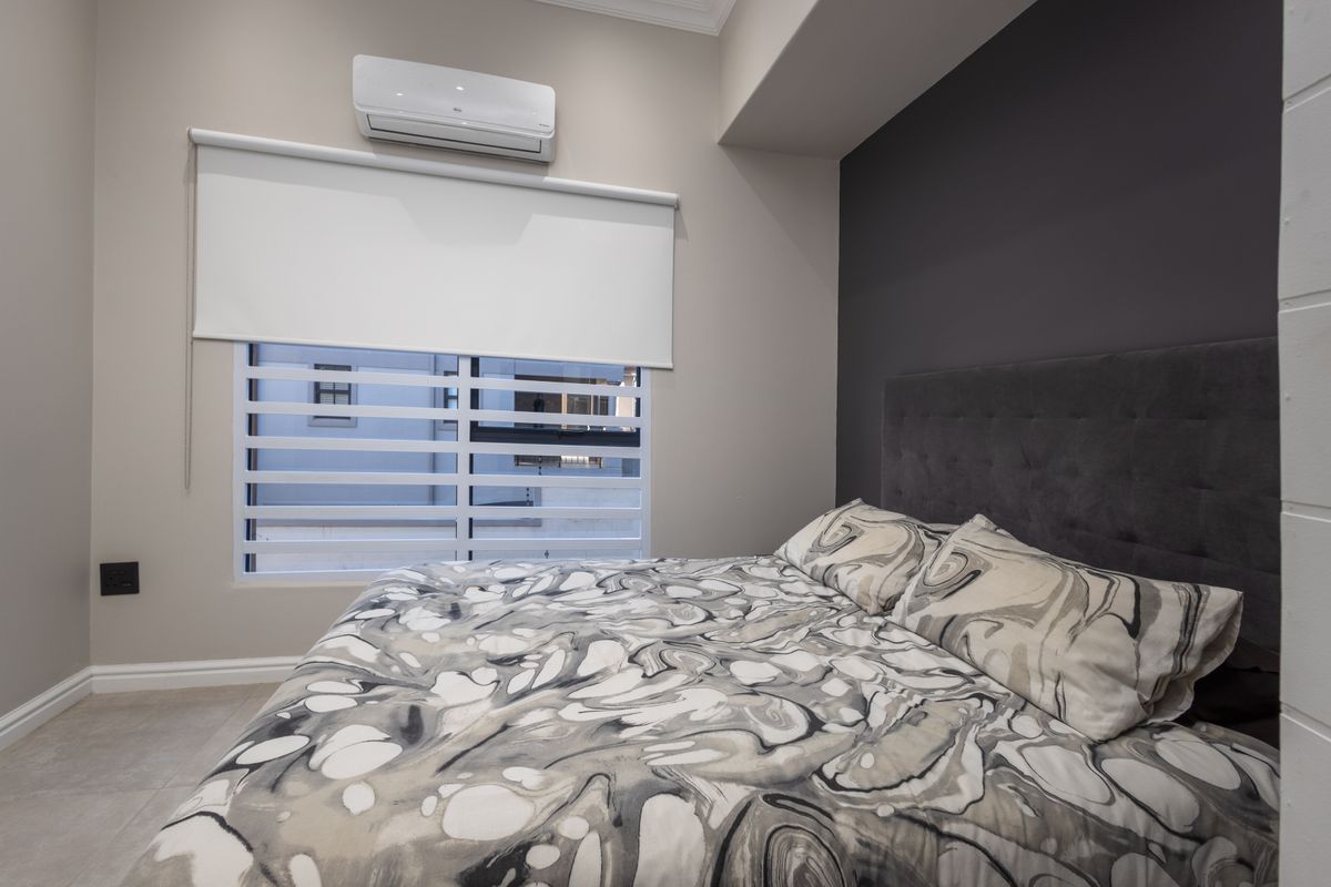 A modern bedroom featuring a dark accent wall, split-system air conditioning, and contemporary window treatments with roller blinds.