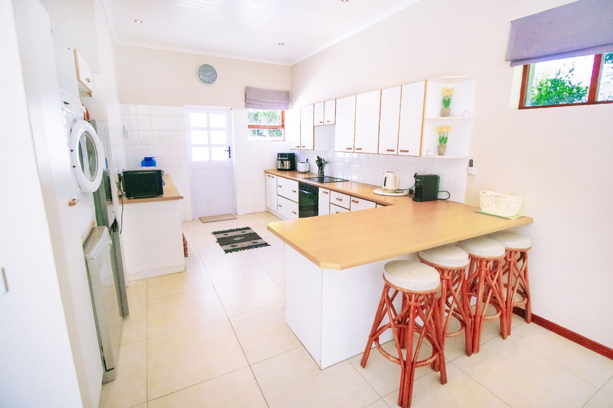 A functional kitchen featuring white cabinetry, light wood-look countertops, a breakfast bar, and integrated oven and hob, with tiled flooring throughout.