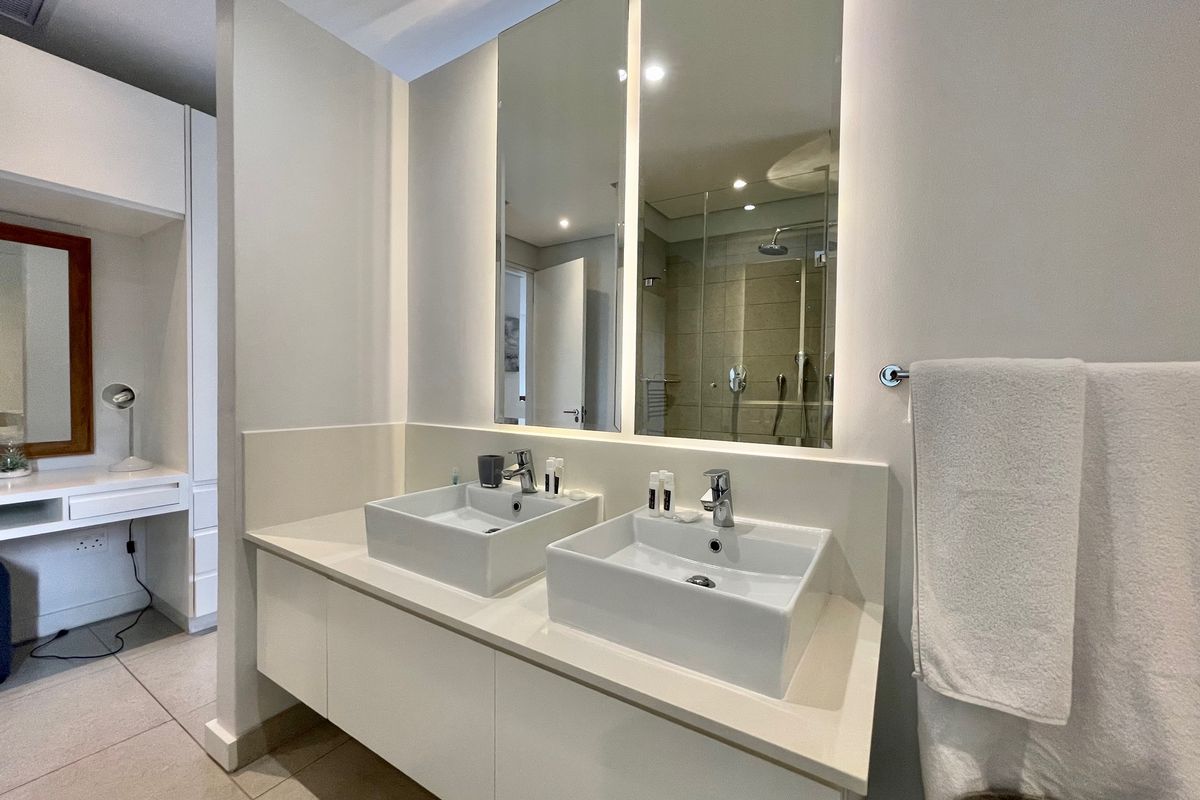 Modern bathroom featuring a double vanity with vessel sinks, integrated LED-lit mirrors, and a walk-in shower with glass enclosure.