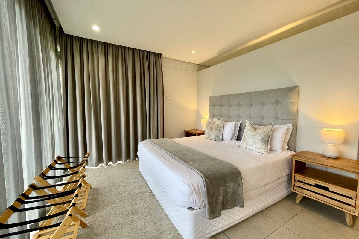 A well-maintained bedroom featuring a tufted headboard, recessed ceiling lighting, and floor-to-ceiling curtains providing access to the exterior.