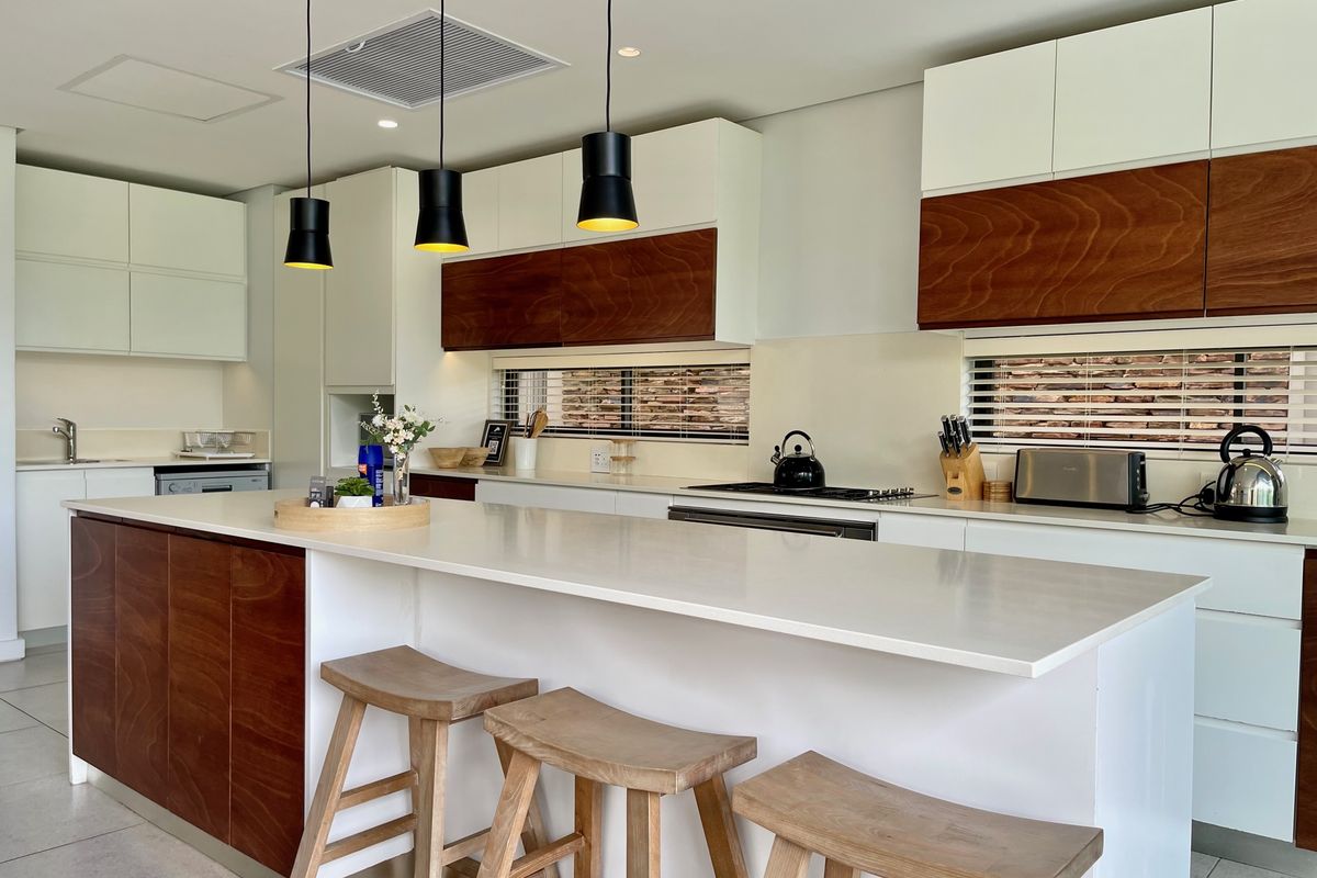 Modern kitchen featuring a large central island with stone countertops, two-tone cabinetry, integrated appliances, and stylish pendant lighting.
