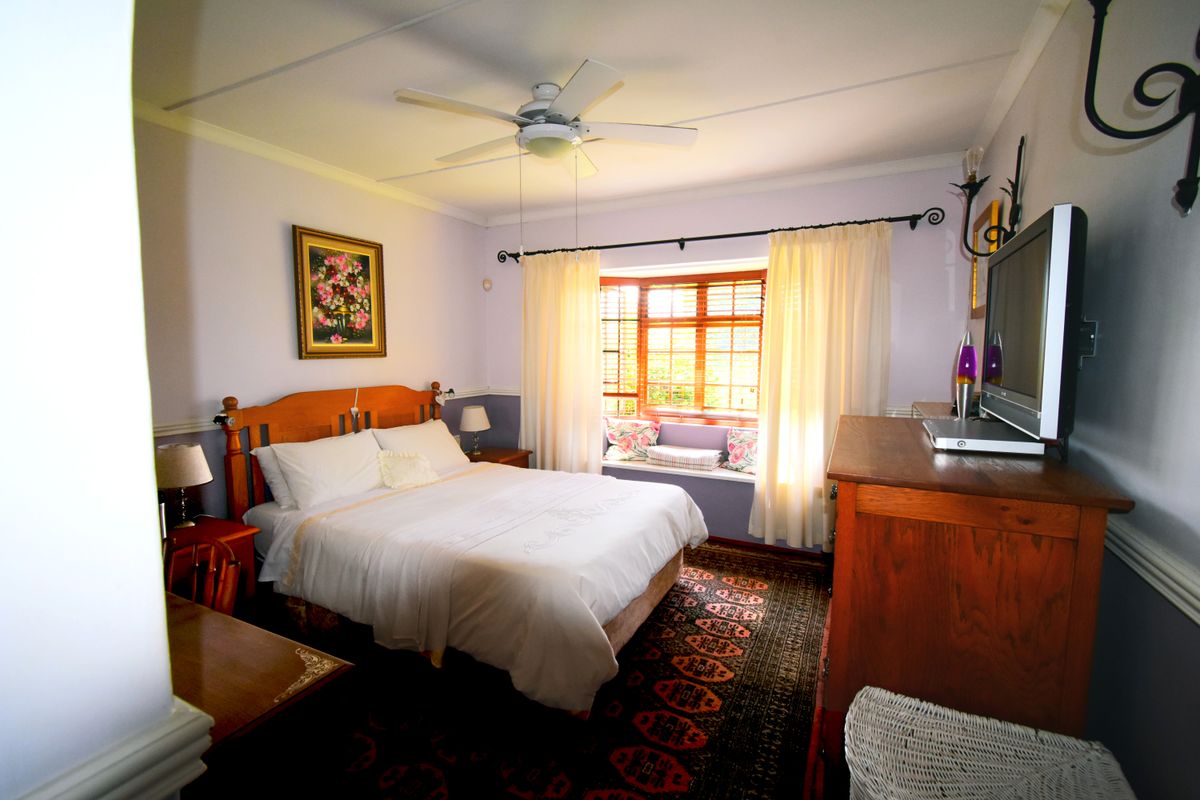 A cozy bedroom featuring a built-in window seat, timber window frames, and a ceiling fan, offering a comfortable and traditional living space.