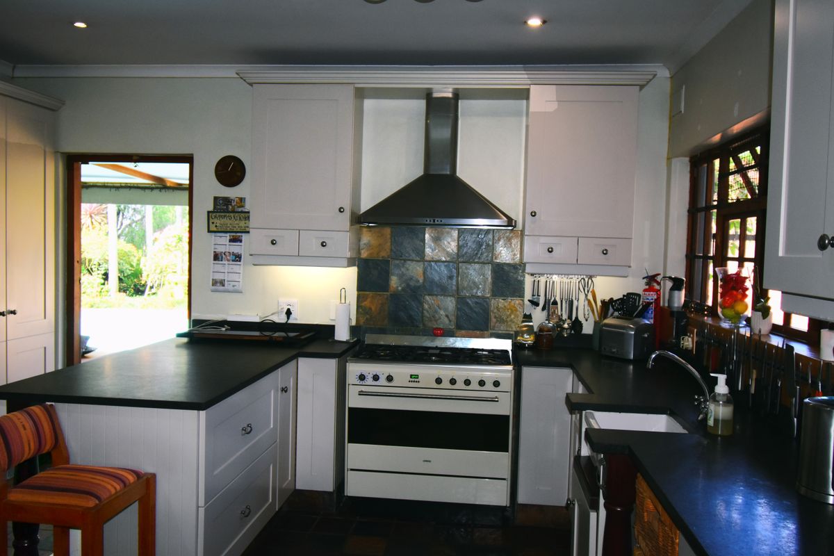 A functional kitchen featuring white cabinetry, dark stone countertops, a gas stove with stainless steel extractor, and a decorative slate tile splashback.