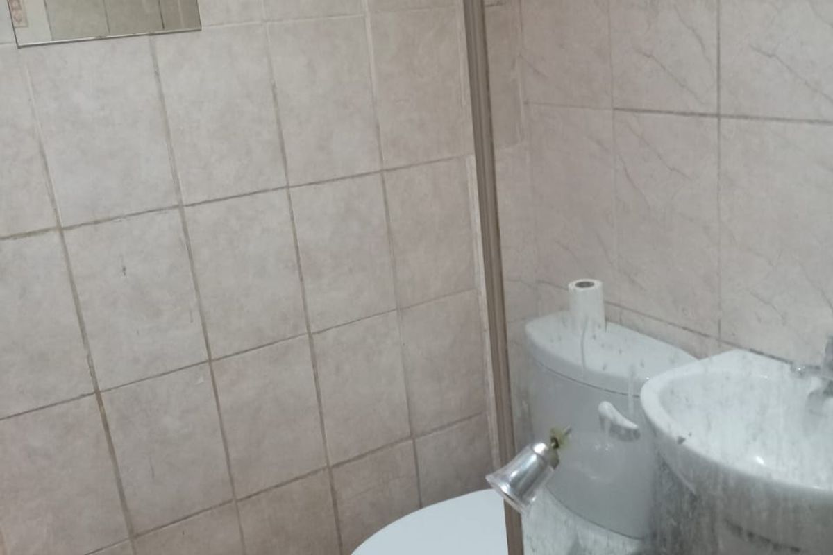 A compact bathroom featuring a pedestal basin, toilet, and a glass-enclosed shower area with tiled walls and flooring.