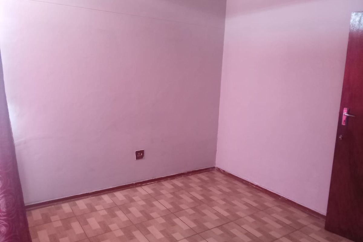 An empty bedroom featuring tiled flooring and a wooden door, providing a blank canvas for personalization.