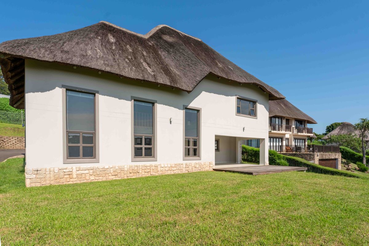 Rear view of a townhouse featuring a traditional thatch roof, stone cladding accents, and a timber deck overlooking a grass lawn.