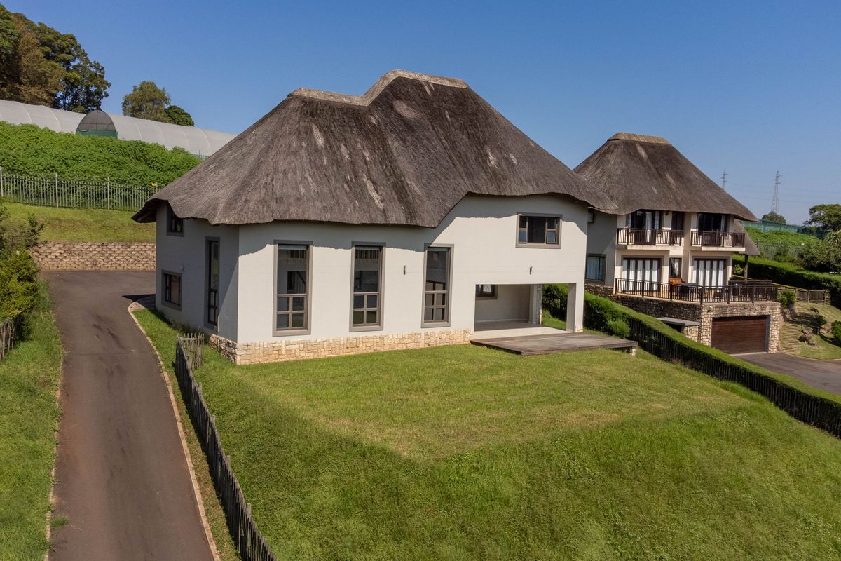 Aerial view of a townhouse featuring a traditional thatch roof, stone base detailing, and a private timber deck overlooking the lawn.