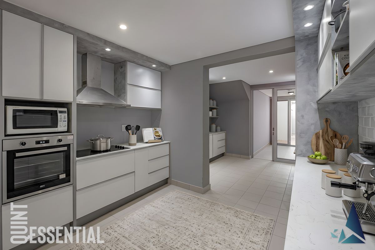 Modern kitchen featuring sleek cabinetry, integrated oven and microwave, induction hob with extractor fan, and stone countertops, leading into a functional scullery area.
