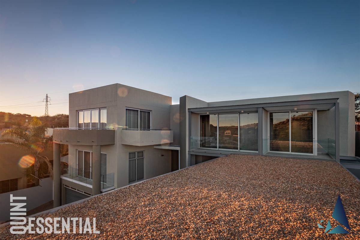 Modern multi-level architectural residence featuring clean lines, large glass sliding doors, glass balustrades, and a gravel-finished flat roof terrace.