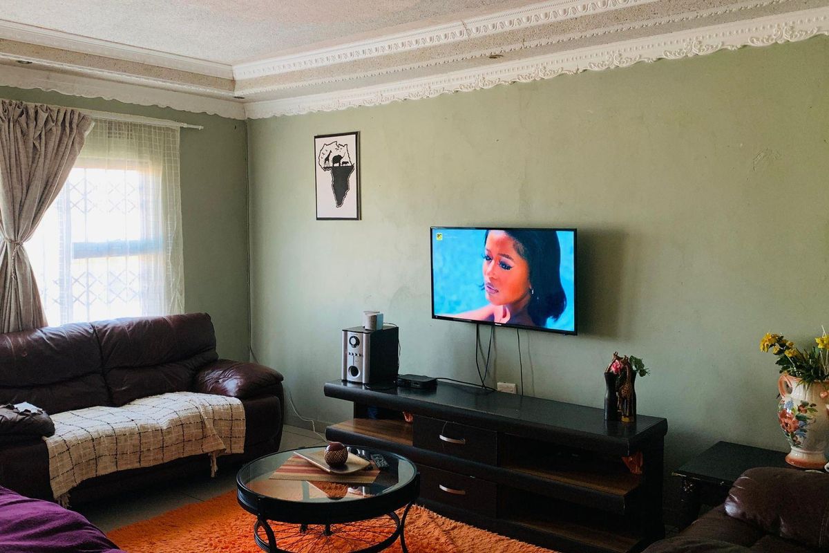 A living room featuring decorative ceiling cornices and an exposed brick pillar, with visible wall surface imperfections requiring cosmetic attention.