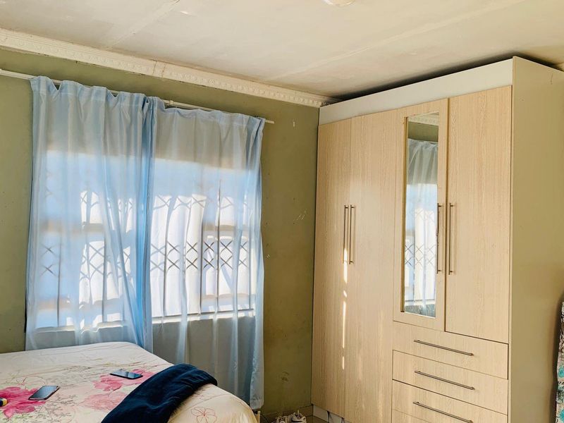 A bedroom featuring a built-in wardrobe, security bars on the window, and decorative ceiling cornice. The walls show signs of wear and paint damage.