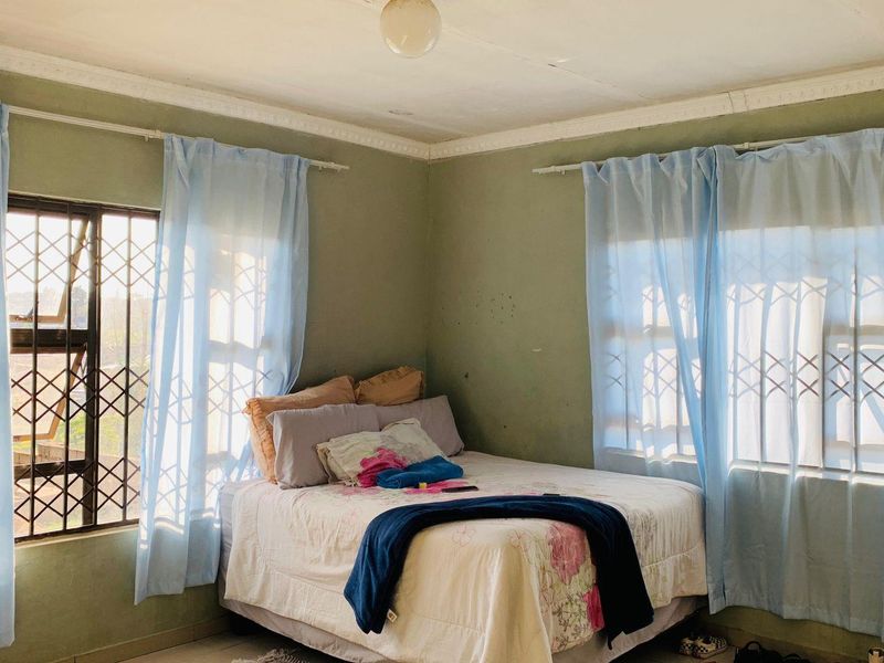 A bedroom featuring tiled flooring, crown molding, and security bars on the windows. The room requires cosmetic updates to the walls and ceiling.