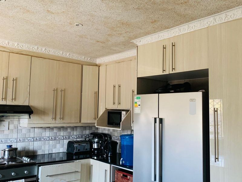 A functional kitchen featuring built-in cabinetry, granite countertops, and a tiled backsplash, currently showing signs of wear on the ceiling and cabinet finishes.