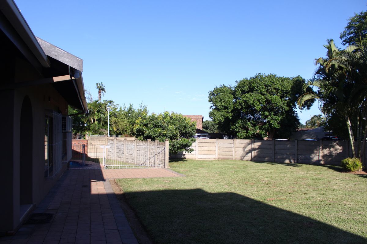 A spacious rear garden featuring a paved patio area, a well-maintained lawn, and secure precast concrete boundary walls.