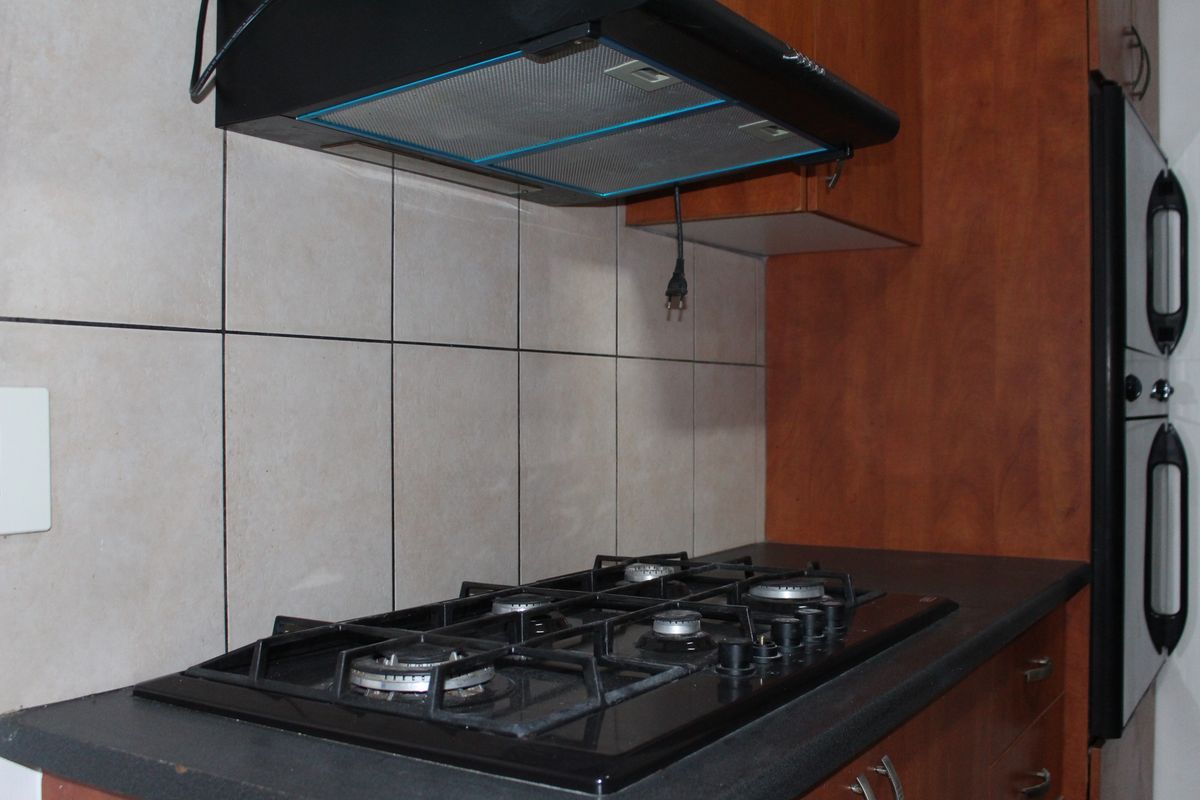 Kitchen area featuring a built-in gas hob, extractor fan, and wall-mounted oven with wooden cabinetry and tiled splashback.