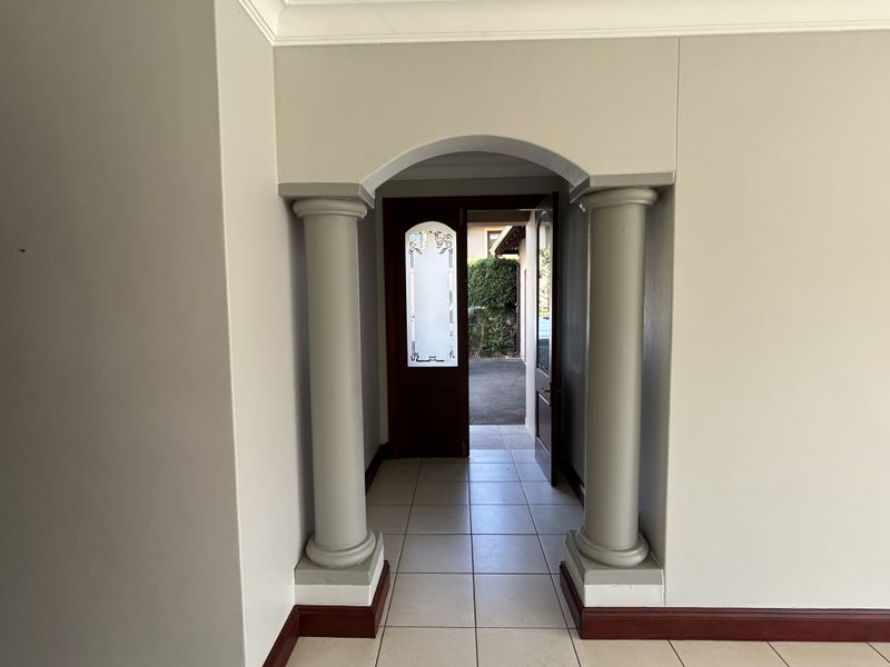 An inviting entrance hall featuring an arched doorway with decorative columns, tiled flooring, and a classic leaded glass front door.