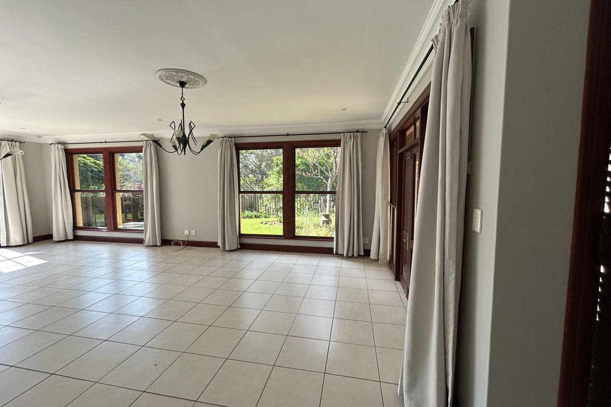 Spacious, light-filled living area featuring neutral tiled flooring, classic ceiling rose, and large timber-framed windows overlooking the garden.