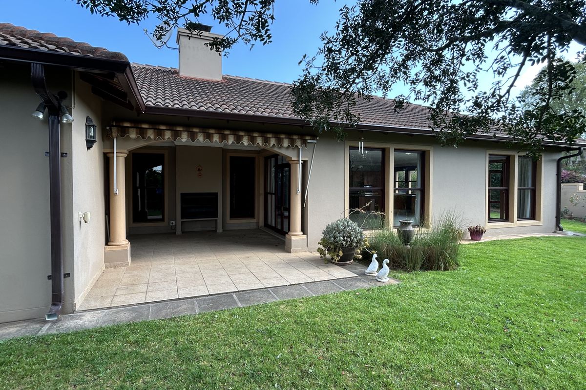 A well-maintained rear exterior featuring a covered tiled patio with a built-in braai, retractable awning, and direct access to a landscaped garden.