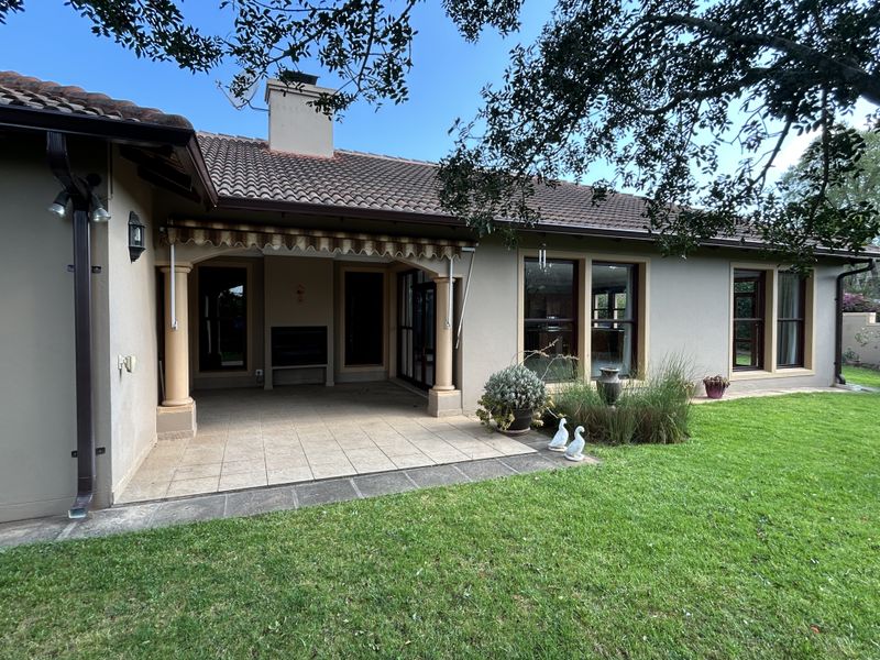 A well-maintained rear exterior featuring a covered tiled patio with a built-in braai, retractable awning, and direct access to a landscaped garden.