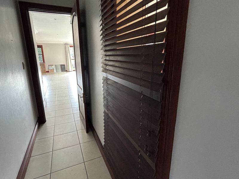 A tiled hallway leading into an open-plan living area, featuring timber door frames and installed venetian blinds.