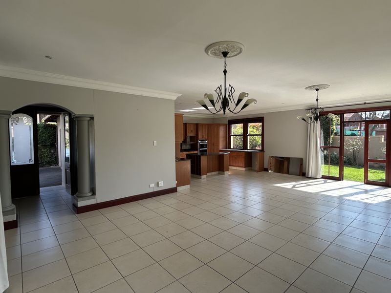 Spacious open-plan living and kitchen area featuring ceramic floor tiles, built-in wooden cabinetry, and direct access to the rear garden through sliding glass doors.