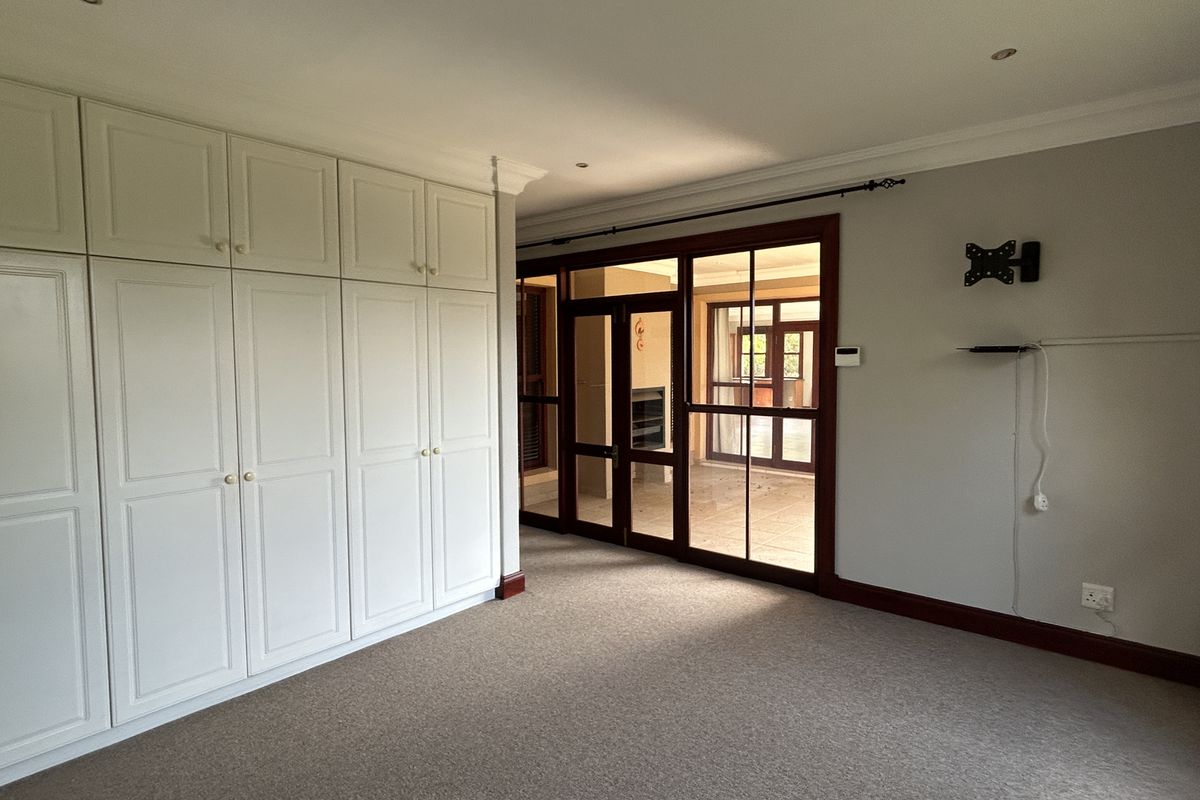 Spacious bedroom featuring extensive built-in cabinetry, neutral carpeting, and large timber-framed glass doors providing access to an adjoining living space.