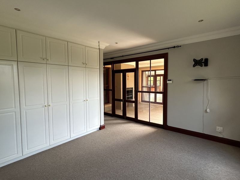 Spacious bedroom featuring extensive built-in cabinetry, neutral carpeting, and large timber-framed glass doors providing access to an adjoining living space.
