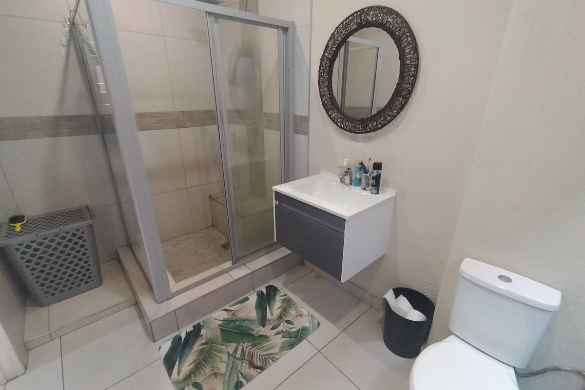 A modern bathroom featuring a glass shower enclosure, a wall-mounted vanity unit, and a standard toilet with neutral tiled finishes.