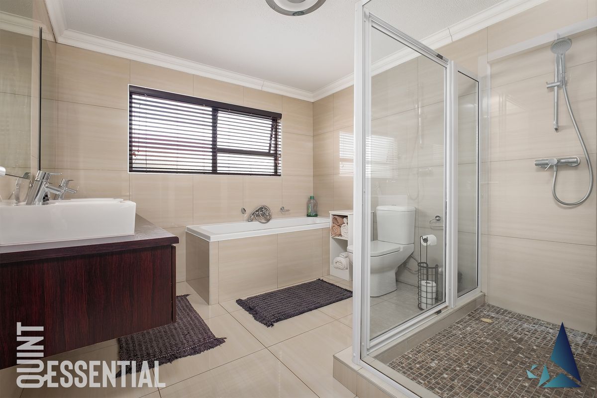 A modern bathroom featuring a glass-enclosed shower, a built-in bathtub, a vanity with a basin, and neutral wall-to-floor tiling.