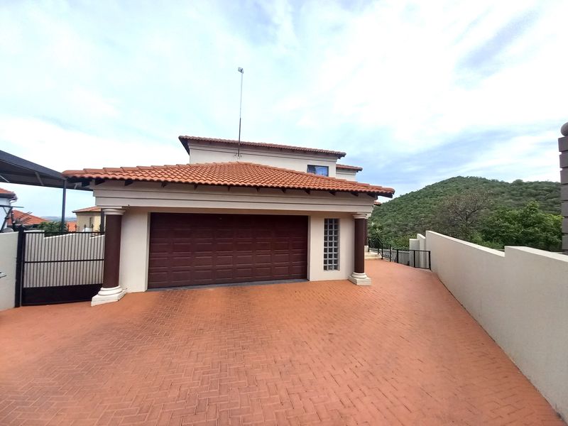 Front exterior view of the property featuring a double garage with a paved driveway, tiled roof, and decorative architectural columns.