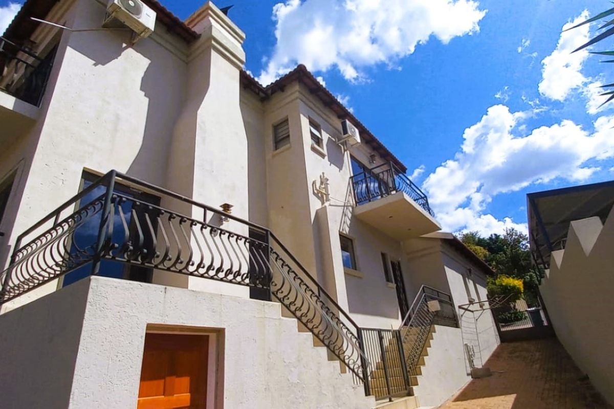 Rear exterior view of a multi-story house featuring wrought iron balcony railings, external staircase, and paved driveway access.