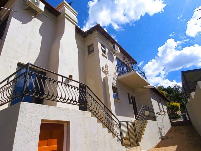Rear exterior view of a multi-story house featuring wrought iron balcony railings, external staircase, and paved driveway access.